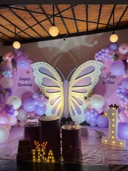 A beautiful butterfly theme for a first birthday, featuring a large, illuminated butterfly centerpiece against a soft purple backdrop and balloon clouds.