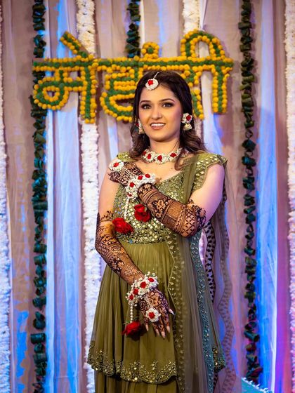 A portrait of the bride at her Mehendi ceremony, dressed in a lovely green outfit with floral jewelry.