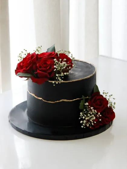 A dramatic black cake for a 60th birthday, featuring a fault line design with a touch of gold and adorned with deep red roses for a classic and romantic feel.