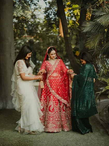 A bride in her red lehenga shares a moment with her bridesmaids, who are helping her with her kalire.