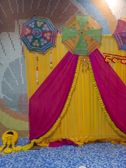 A poolside Haldi setup with a backdrop of yellow and pink drapes, decorated with Rajasthani umbrellas. The colorful mosaic tiles of the pool area complement the festive decor.