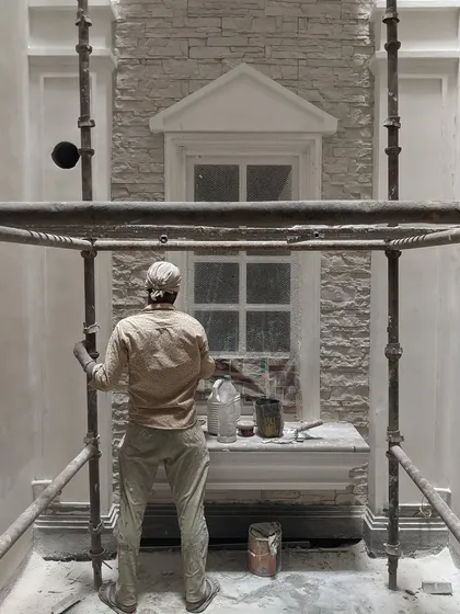 A craftsman at work inside the open-to-sky shaft of the KAIRA residence. This image captures the skilled labor involved in executing the detailed rubble masonry and classical mouldings.
