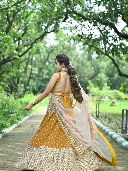 A back view of the mustard yellow lehenga, showcasing the low-back blouse design and the flow of the sheer dupatta.