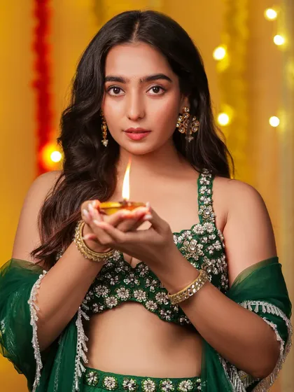 A classic Diwali portrait of a model holding a lit diya, looking directly at the camera with a warm and inviting expression.
