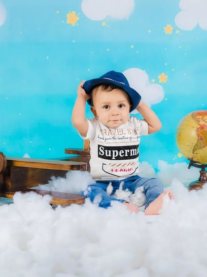 A baby boy adjusts his hat, looking like a cool and confident little pilot.