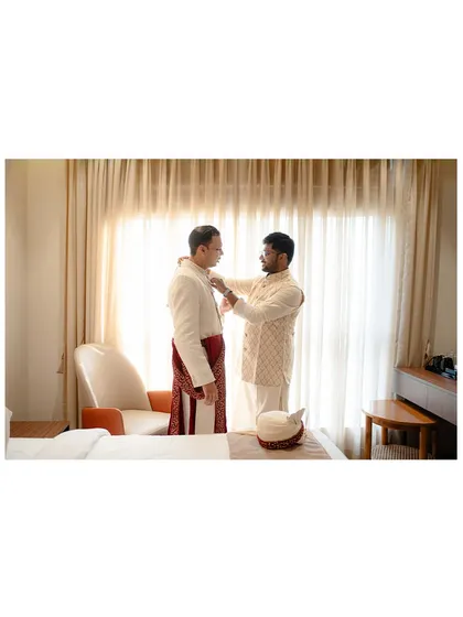 The groom getting help with his attire, a moment of camaraderie and preparation before the Bengali rituals.