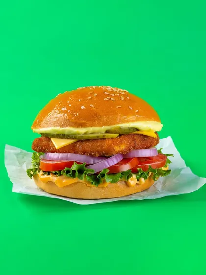 A classic chicken burger with fresh lettuce, tomato, and onion, shot for Bistro by Blinkit's online menu. The solid green background makes the product the sole focus.