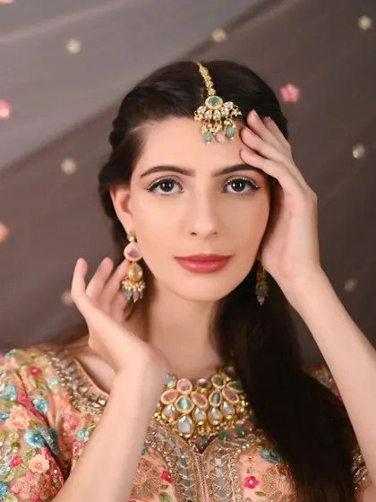 A close-up on the model's stunning makeup and the intricate, multi-colored jewellery that perfectly complements the peach lehenga.
