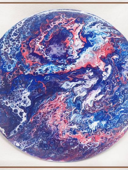 A circular resin art piece with a striking resemblance to a planet or a nebula, created using blue, red, and white pigments.