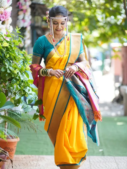 A full-length shot of the bride in her yellow Nauvari, perfect for the Vidhi ceremony. The outdoor lighting showcases the natural, glowing finish of the makeup.