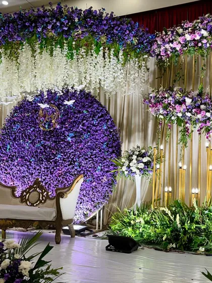 For this monsoon wedding reception, we designed a romantic stage drenched in shades of purple. A massive circular backdrop of purple chrysanthemums, paired with hanging white wisteria and lush greenery, creates a dreamy, immersive floral experience.