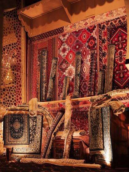 A full view of the rug market stall, with carpets hung as backdrops and rolled up for display, creating the feel of a real merchant's shop.