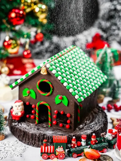 An intricate gingerbread house with a green roof, with "snow" falling in the foreground. This magical shot captures the wonder and detail of classic Christmas baking.