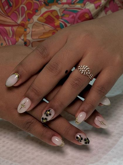 This 'blueming' nail art features delicate, hand-painted black flowers with gold centers over a milky white base. The gold French tip adds a touch of luxury.