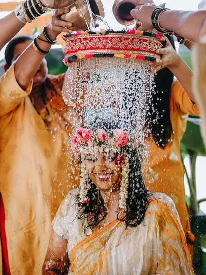 A traditional and joyful moment from a Haldi ceremony. The bride is showered with rice and water, a beautiful ritual captured in a burst of motion and genuine smiles.