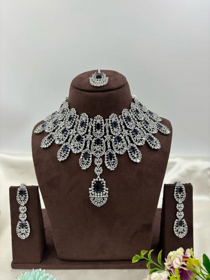 A full-coverage AD bridal set with a matching maang tikka. This silver-plated design is available in a wide range of colors like green, blue, pink, and white, making it a versatile choice for weddings.