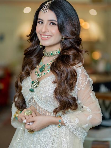 A close-up portrait that captures the bride's radiant smile and the exquisite details of her emerald jewelry against the soft ivory fabric.