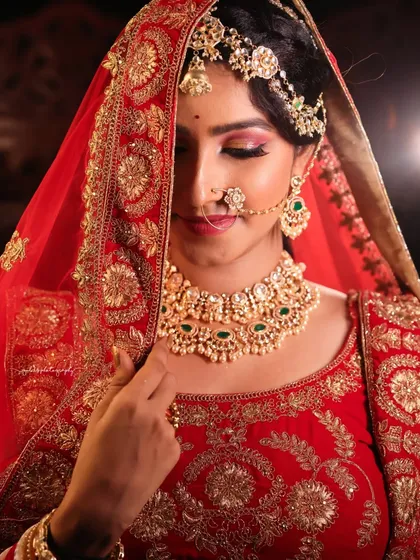 The bridal veil or dupatta adds a layer of tradition and mystery. This shot captures the bride adjusting her veil, with the rich red and gold embroidery framing her face beautifully.