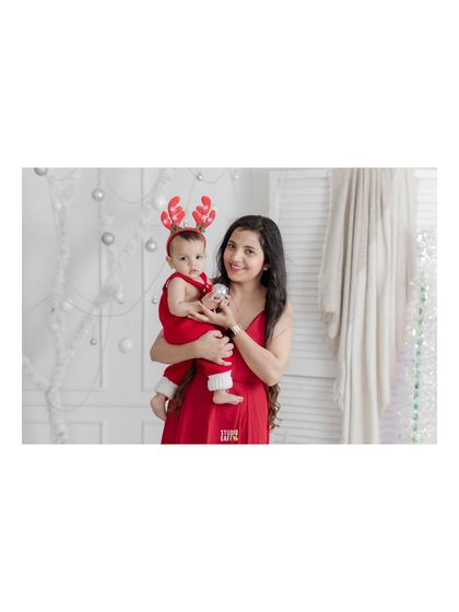 A mother and her baby, both in festive red, share a moment during their Christmas shoot.