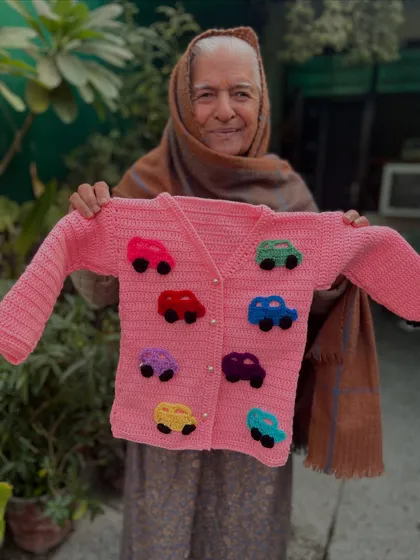 For the little car enthusiast. This pink cardigan is decorated with colorful, puffy crochet cars. It's a playful design that adds a pop of fun to a classic button-up sweater.