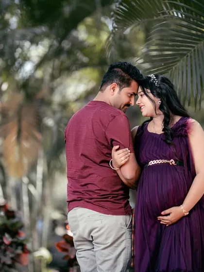 An intimate moment during a maternity shoot. The deep purple ruffled gown adds a touch of royalty and elegance to this couple's portrait amidst lush greenery.