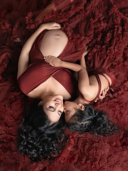 An artistic maternity portrait celebrating the beautiful bond between a mother and her daughter. The rich red fabric creates a dramatic and loving scene as they wait for the new arrival.