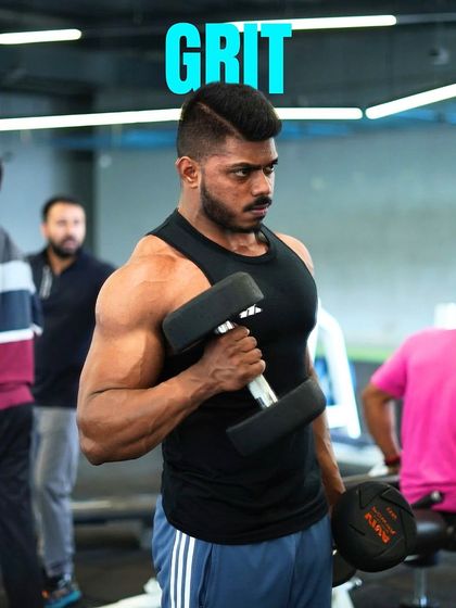 Grit is what it takes. A member with impressive bicep development performs a focused dumbbell curl, showing the intensity of his training.