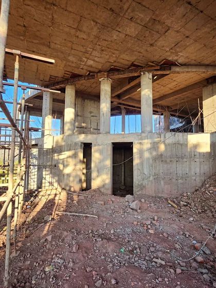 An interior view of the construction site, showing the concrete columns and floor slabs that form the building's skeleton. The open design allows for uninterrupted sightlines through the space and out towards the hills.