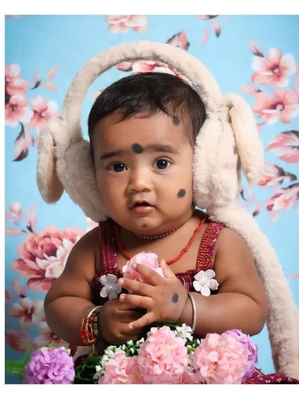 A beautiful portrait of a baby girl holding a pink flower. The soft colors of the flowers and the floral background create a gentle and coordinated look.