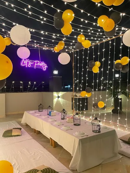 We can turn any terrace into a chic party lounge. This nighttime birthday setup features a canopy of fairy lights, hanging paper lanterns, low seating with a central table, and a "Let's Party" neon sign for a cool, celebratory vibe.