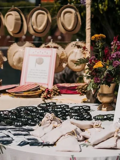 A fun and practical favor station for a sunny outdoor event. I set up a table with hats and sunglasses for guests, with a playful sign that reads 'Don't be BLINDED by our Love'.