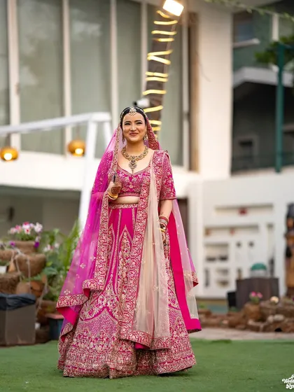 A beautiful outdoor portrait of the bride, her vibrant pink lehenga standing out against the natural background.