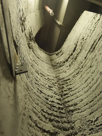 A detail view looking up into a narrow, textured concrete crevice within the store. This demonstrates the construction technique used to achieve the cave-like, excavated quality of the space, focusing on raw materiality.