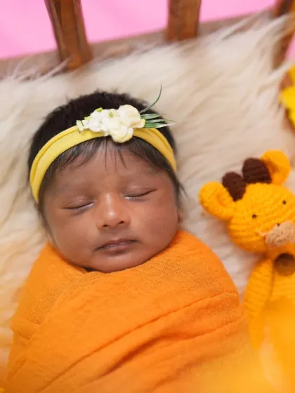 A sweet newborn wrapped in a sunny orange swaddle sleeps next to a small crocheted giraffe toy. The bright color and simple props create a cheerful and adorable image.