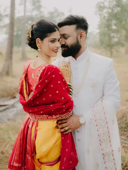 An intimate embrace during an outdoor pre-wedding shoot. The focus is on their close connection, with the bride's vibrant red and yellow saree adding a beautiful pop of color.