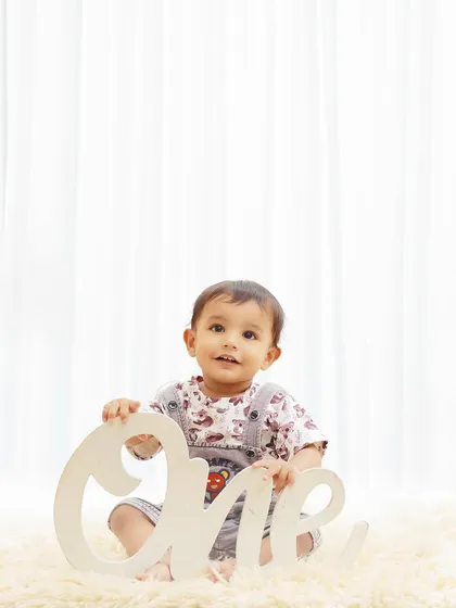 Simple and classic can be just as beautiful. This indoor studio shot uses a clean, white background and a fluffy rug to keep all the focus on the birthday boy and his "One" sign.