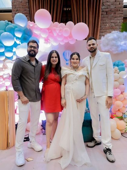 The parents-to-be with their friends, all smiles in front of the 'Up, Up & Away' themed decor.