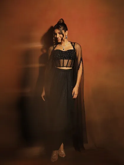 A full-length shot of this stunning cocktail party look. The makeup is fresh and modern, with a focus on glowing skin that stands out against the all-black ensemble.