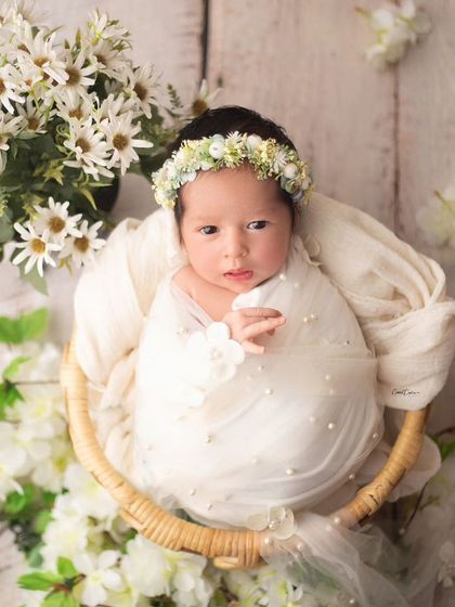 A basket of beauty. This awake baby girl is nestled among white flowers, creating a fresh and angelic portrait with a rustic touch.
