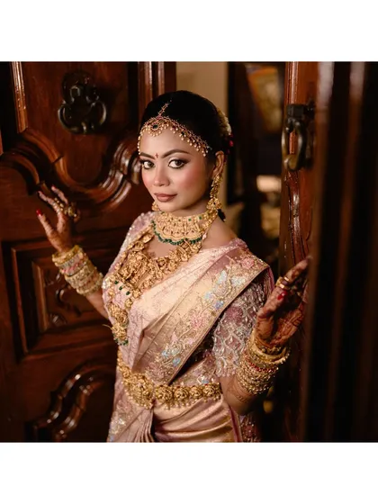A bride, adorned in stunning gold jewelry, peeks out from behind a heavy wooden door, a classic and elegant bridal portrait.