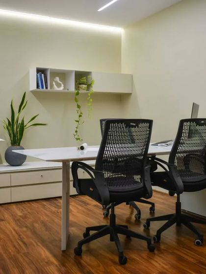 The second director's cabin, featuring a minimalist aesthetic with clean white surfaces and warm wood flooring. Floating shelves and simple decor keep the space feeling open and focused.