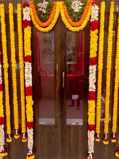 A traditional housewarming flower decoration for a home door. The entrance is framed with yellow marigold and white jasmine flower garlands.