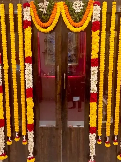 A traditional housewarming flower decoration for a home door. The entrance is framed with yellow marigold and white jasmine flower garlands.