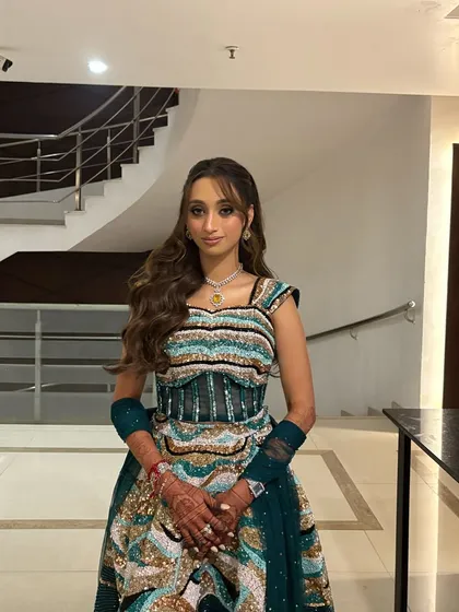 A full-length view of the client's Sangeet look, with her hair in soft waves and face-framing bangs, complementing her unique, colorful outfit.
