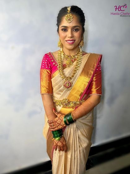A full-length view of Kavya's elegant bridal look. The antique gold jewellery, including the vaddanam, perfectly complements her cream and pink Kanjeevaram saree.