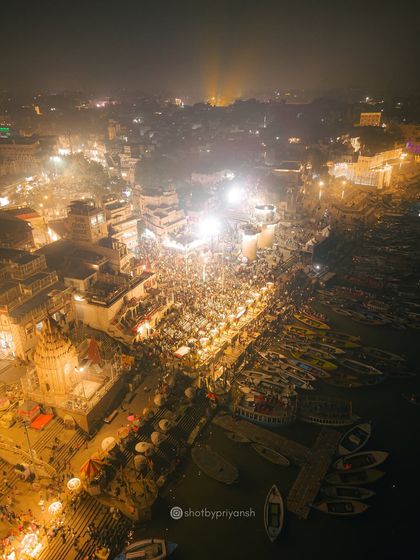 A wider aerial view of the Ganga Aarti ceremony at Varanasi. The drone reveals the scale of the gathering and the river dotted with countless boats.