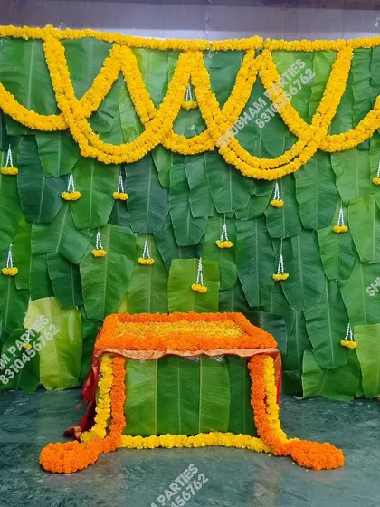 A classic and vibrant backdrop for a traditional Indian ceremony, such as a puja or Simmanta. This decoration is made entirely of fresh banana leaves and decorated with beautiful marigold flower garlands, creating an authentic and auspicious setting.