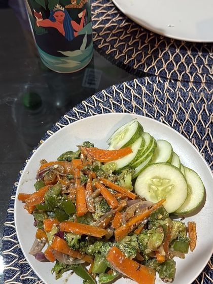 A plate of stir-fried broccoli, carrots, and bell peppers with a side of cucumber slices. A light and crunchy meal packed with nutrients.