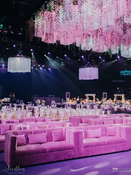 Rows of plush pink sofas provided comfortable and stylish seating for guests. Above, a massive ceiling installation of hanging flowers and fringe added texture and drama to the vast space.