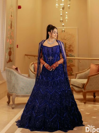 A client wears a fully embellished corset lehenga in a striking active blue. The voluminous skirt and structured bodice create a look that is bold, modern, and timeless.